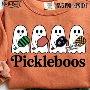 May include: Orange sweatshirt featuring four white ghost characters holding pickleball paddles in green, red, black, and yellow. The word "Pickleboos" is printed in black script below the ghosts. The sweatshirt has a crew neck.
