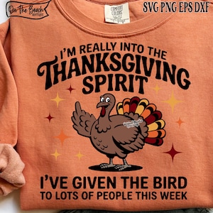 May include: Orange sweatshirt with the text "I'M REALLY INTO THE THANKSGIVING SPIRIT" and "I'VE GIVEN THE BIRD TO LOTS OF PEOPLE THIS WEEK". A cartoon turkey with colorful feathers is featured in the center. The sweatshirt has a crew neck.