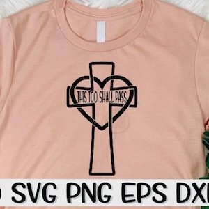 May include: A light peach-colored t-shirt featuring a black graphic of a cross intertwined with a heart shape. The text "THIS TOO SHALL PASS" is centered within the heart. The bottom of the shirt displays the text "SVG PNG EPS DXF".