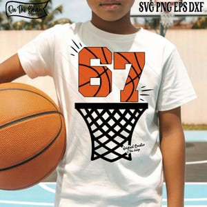 May include: A white t-shirt featuring a basketball-themed design. The design includes the number "67" in orange, with a basketball texture, above a black basketball net. A basketball is held in the person's left arm.