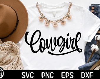 May include: White t-shirt with the word "Cowgirl" written in black cursive script. The shirt is laying on a table with a brown hat, a crocheted sweater, a pair of jeans, and a cotton plant.