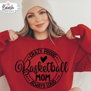 Puede incluir: Una sudadera roja con un diseño circular negro que dice "Crazy Proud... Basketball Mom... Always Loud".