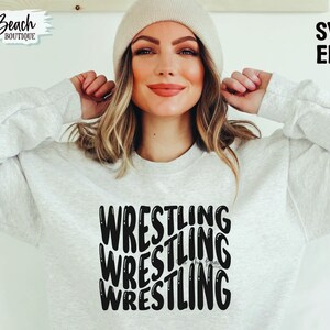 May include: A white sweatshirt with the word "WRESTLING" repeated four times in a stacked, overlapping design. The text is in black and has a slightly distressed look.