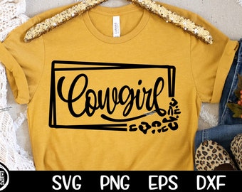 Könnte beinhalten: Ein senfgelbes T-Shirt mit einer schwarzen Grafik, auf der in einer stilisierten Schrift "Cowgirl!" steht. Die Grafik ist von einem schwarzen Rechteck und einem Muster aus schwarzen Leopardenflecken umgeben.