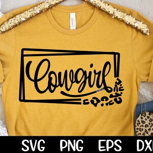 May include: A mustard yellow t-shirt with a black graphic that says "Cowgirl!" in a stylized font. The graphic is surrounded by a black rectangle and a pattern of black leopard spots.