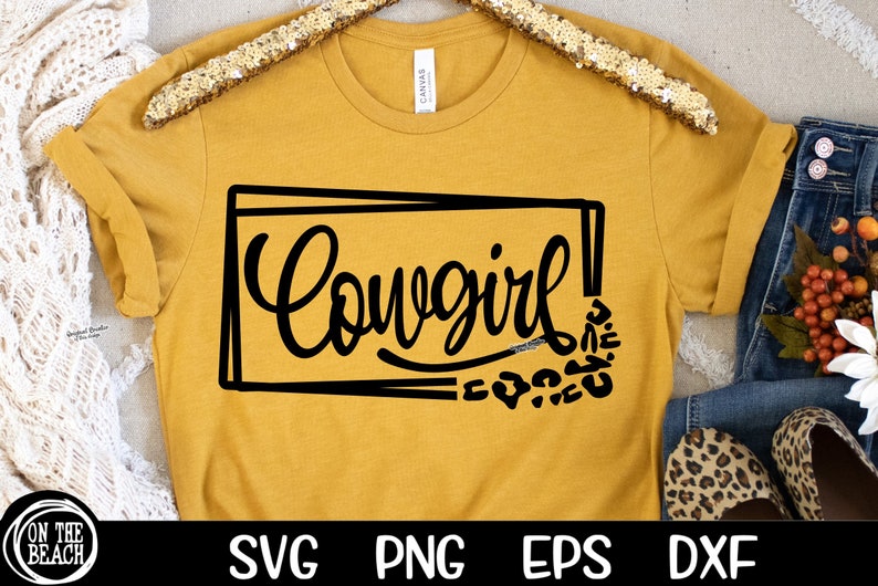 May include: A mustard yellow t-shirt with a black graphic that says "Cowgirl!" in a stylized font. The graphic is surrounded by a black rectangle and a pattern of black leopard spots.