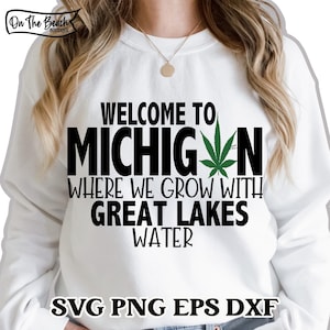 Op de afbeelding: Wit sweatshirt met zwarte tekst die "Welkom in Michigan Waar we groeien met Great Lakes Water" luidt en een groene marihuana-bladgrafiek. De tekst "SVG PNG EPS DXF" staat onderaan de afbeelding.