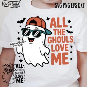May include: White t-shirt featuring a cartoon ghost wearing sunglasses and a baseball cap. The text "ALL THE GHOULS LOVE ME" is printed in orange. Black bats and stars surround the ghost, perfect for Halloween.