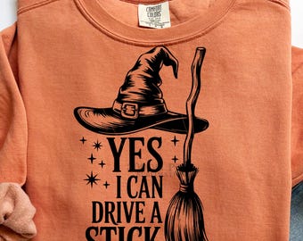 Könnte beinhalten: Orangefarbenes Comfort Colors Sweatshirt mit schwarzer Grafik eines Hexenhuts, Besens und dem Text "YES I CAN DRIVE A STICK". Perfekt für Halloween.