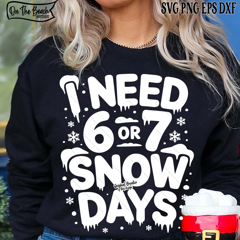 May include: Black sweatshirt with the text "I NEED 6 OR 7 SNOW DAYS" in white. The design includes snowflakes and icicles. The sweatshirt has the "On The Beach Boutique" logo in the upper left corner.