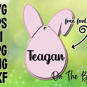 May include: Pink bunny-shaped Easter egg with a hole for hanging. The egg has the name "Teagan" written on it in black cursive font. The text "On The Beach Boutique" is written below the egg in black cursive font.
