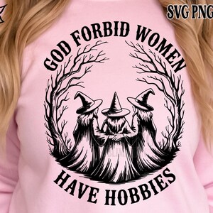 May include: A light pink sweatshirt featuring a black graphic of three witches in pointed hats, surrounded by a tree-like design. The text reads "GOD FORBID WOMEN HAVE HOBBIES" in a circular arrangement. The top right corner has the text "SVG PNG EPS DXF".