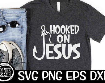 Peut inclure: Un t-shirt gris foncé avec un crochet blanc et le texte "Hooked on Jesus" imprimé sur le devant. Le t-shirt est présenté sur un fond blanc avec un jean, des lunettes de soleil et des baskets.