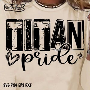 May include: Cream-colored long-sleeve shirt with the words "TITAN pride" in black, distressed font. A heart graphic and a hashtag symbol are included in the design. The shirt also has the text "SVG PNG EPS DXF".
