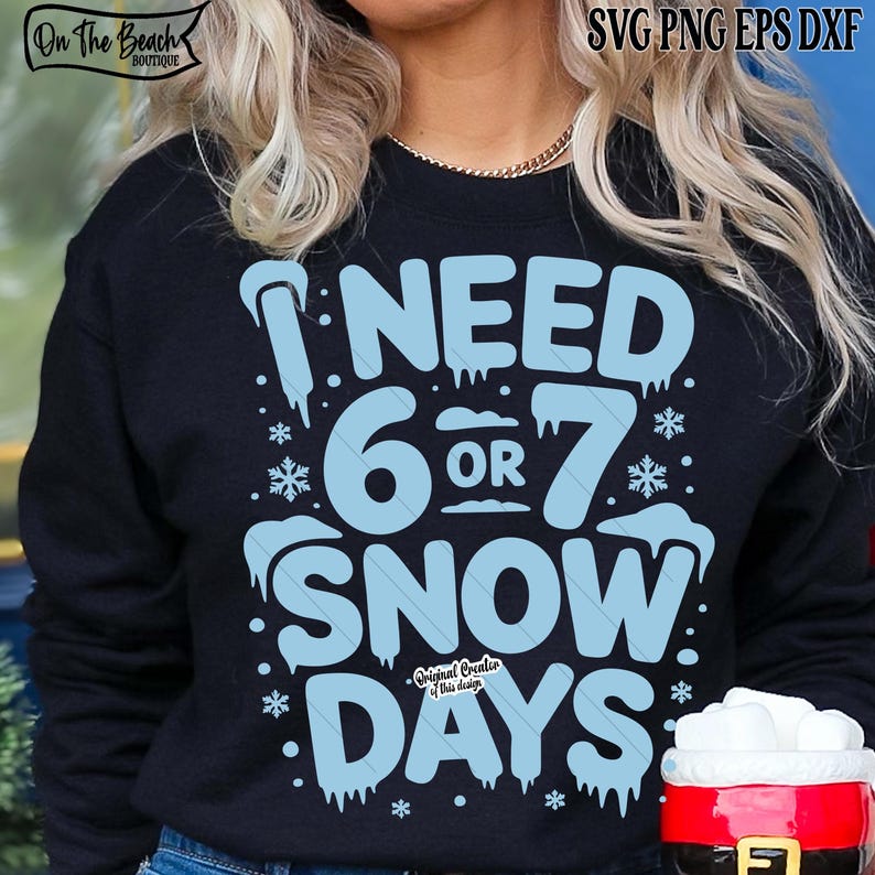 May include: A navy blue sweatshirt with the text "I NEED 6 OR 7 SNOW DAYS" in light blue. The design includes snowflakes and icicles. The sweatshirt has the text "On The Beach Boutique" at the top left.