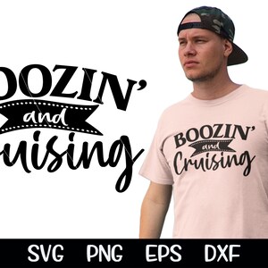 May include: A pink t-shirt with the text "Boozin' and Cruising" in black. The text is in a stylized font with a banner underneath. The shirt is being worn by a person with a camouflage baseball cap.