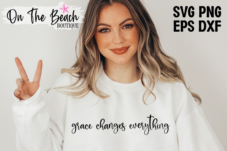 May include: A white sweatshirt with the text "grace changes everything" in black cursive lettering. The model is wearing the sweatshirt and giving a peace sign.