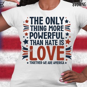 May include: White t-shirt with the text "THE ONLY THING MORE POWERFUL THAN HATE IS LOVE" in navy blue and red. The design includes stars and stripes, with the words "TOGETHER-WE ARE AMERICA" at the bottom.