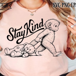 Pode incluir: T-shirt rosa claro com um gráfico preto de um macaco e um ursinho de pelúcia, com a frase "Stay Kind" acima. A camiseta tem gola redonda e mangas curtas. A imagem também inclui o texto "SVG PNG EPS DXF".