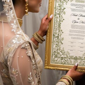 May include: A bride holds a framed wedding certificate with a floral border. The certificate is for Noah Ibrahim and Elyza Noor. The bride is wearing a white and gold embroidered dress and a veil.