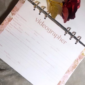 Puede incluir: Una carpeta blanca con un dise&ntilde;o floral rosa y dorado. La carpeta tiene un t&iacute;tulo que dice "vide&oacute;grafo" e incluye un formulario para registrar informaci&oacute;n de video.