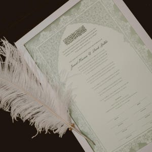 Może przedstawiać: Pi&oacute;ro z białego pi&oacute;ra leży na białym oprawionym dokumencie z zielonym tłem. Dokument to akt małżeństwa z tekstem "This document solemnly certifies that the marriage of Janoud Hussain & Sarah Balki" w czarnym kolorze.
