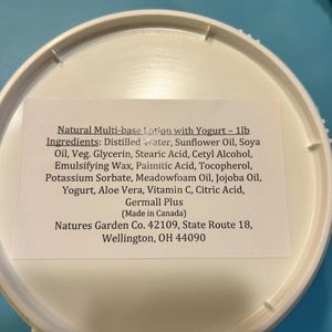 May include: A white plastic container lid featuring a rectangular label that reads: Natural Multi-base Lotion with Yogurt - 1lb. Ingredients: Distilled Water, Sunflower Oil, Soya Oil, Veg. Glycerin, Stearic Acid, Cetyl Alcohol, Emulsifying Wax, Palmitic Acid, Tocopherol, Potassium Sorbate, Meadowfoam Oil, Jojoba Oil, Yogurt, Aloe Vera, Vitamin C, Citric Acid, Germall Plus (Made in Canada) Natures Garden Co. 42109, State Route 18, Wellington, OH 44090.