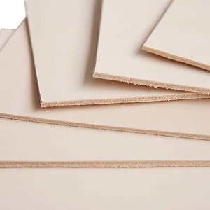May include: A stack of five light beige leather pieces, each with a slightly rough edge.