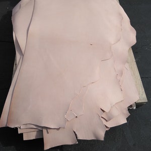 May include: A stack of light pink leather hides, likely for crafting or leatherworking projects.
