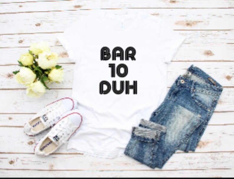 May include: A white t-shirt with the text "BAR 10 DUH" in black, paired with blue jeans and white sneakers. A bouquet of white flowers is also present, creating a casual, everyday look.