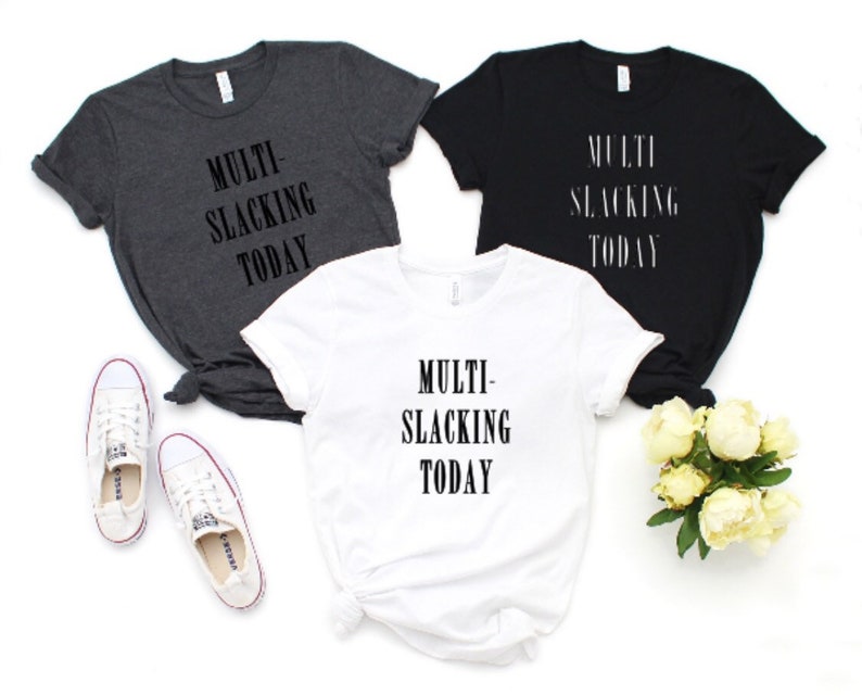Puede incluir: Tres camisetas con el texto "MULTI-SLACKING TODAY" impreso en ellas. Las camisetas son de color gris, negro y blanco.