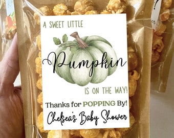 May include: A brown paper bag filled with popcorn and tied with twine. A white tag with green and brown pumpkin illustration and the text "A sweet little Pumpkin is on the way! Thanks for popping by! Chelsea's Baby Shower" is attached to the bag.