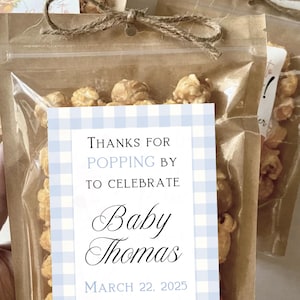 May include: A clear plastic bag filled with caramel popcorn with a blue and white gingham tag that says "Thanks for popping by to celebrate Baby Thomas March 22, 2025".