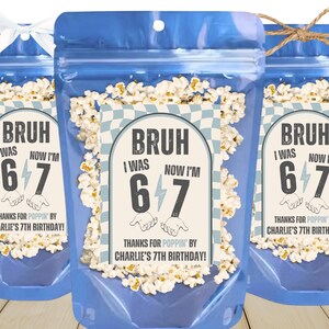 May include: Three blue cellophane bags filled with popcorn. Each bag has a label that reads "BRUH I WAS 6 NOW I'M 7" with the text "THANKS FOR POPPIN' BY CHARLIE'S 7TH BIRTHDAY!" The bags are tied with a white ribbon and twine.