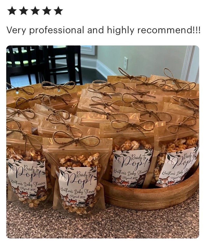 May include: A collection of clear plastic pouches filled with caramel popcorn, each tied with a brown twine bow at the top. The labels feature the text Ready to Pop! Heather's Baby Shower April 2024, decorated with illustrations of woodland animals.