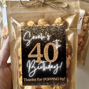 Pu&ograve; includere: Un sacchetto di plastica trasparente pieno di popcorn al caramello con un'etichetta nera e dorata che dice "Sarah's 40th Birthday! Thanks for POPPING by!"