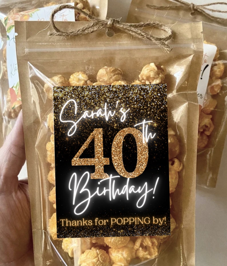 Pu&ograve; includere: Un sacchetto di plastica trasparente pieno di popcorn al caramello con un'etichetta nera e dorata che dice "Sarah's 40th Birthday! Thanks for POPPING by!"