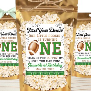 May include: A gold foil pouch filled with popcorn, featuring a label that reads First Year Down! Our Little Rookie Is Turning One. Thanks for Poppin' By, Hope You Had Fun! Kenneth's 1st Birthday May 30, 2026, with a football and field graphic.