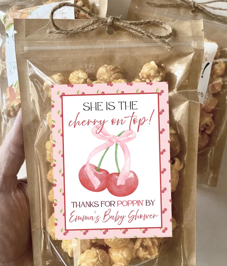 May include: Clear cellophane bag filled with popcorn, tied with twine. A pink label features a cherry illustration and the text "SHE IS THE cherry on top! THANKS FOR POPPIN' BY Emma's Baby Shower."