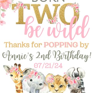 May include: A pink and gold birthday party sign with the text "Born Two be wild" and "Thanks for POPPING by Annie's 2nd Birthday! 07/21/24". The sign features a watercolor illustration of a giraffe, elephant, lion, and zebra wearing flower crowns.