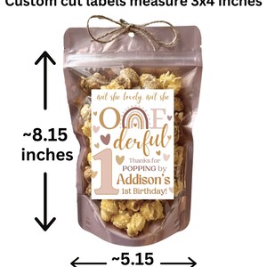 May include: A clear plastic bag filled with popcorn and a pink and brown label that says "One-derful" with a rainbow and hearts. The label also says "Thanks for popping by Addison's 1st Birthday!" The bag is 8.15 inches tall and 5.15 inches wide.