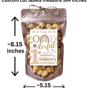 Puede incluir: Una bolsa transparente llena de palomitas de ma&iacute;z, atada con hilo. La bolsa mide aproximadamente 20,7 cm de alto y 13,1 cm de ancho. Una etiqueta dice "One-derful" con el texto "&iexcl;Gracias por POPPING por el 1er cumplea&ntilde;os de Addison!" Las etiquetas miden 7,6 x 10,2 cm.