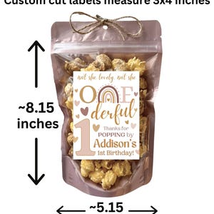 May include: A clear cellophane bag filled with popcorn, tied with twine. The bag has a label that reads "One-derful" with a rainbow and the text "Thanks for POPPING by Addison's 1st Birthday!" The bag measures approximately 8.15 inches tall and 5.15 inches wide.