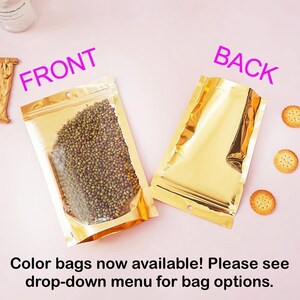 May include: Two gold stand-up pouches with zipper closures. The pouch on the left is filled with green mung beans. The pouch on the right is empty. The text "FRONT" is written above the pouch on the left and the text "BACK" is written above the pouch on the right. The text "Color bags now available! Please see drop-down menu for bag options." is written below the pouches.