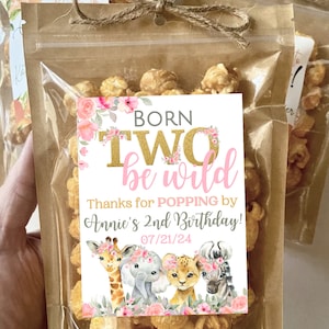 May include: A small clear bag filled with popcorn and tied with twine. A white tag with pink and gold lettering reads "Born Two be wild" and "Thanks for POPPING by Annie's 2nd Birthday! 07/21/24". The tag features a cartoon giraffe, elephant, lion, and zebra with floral accents.