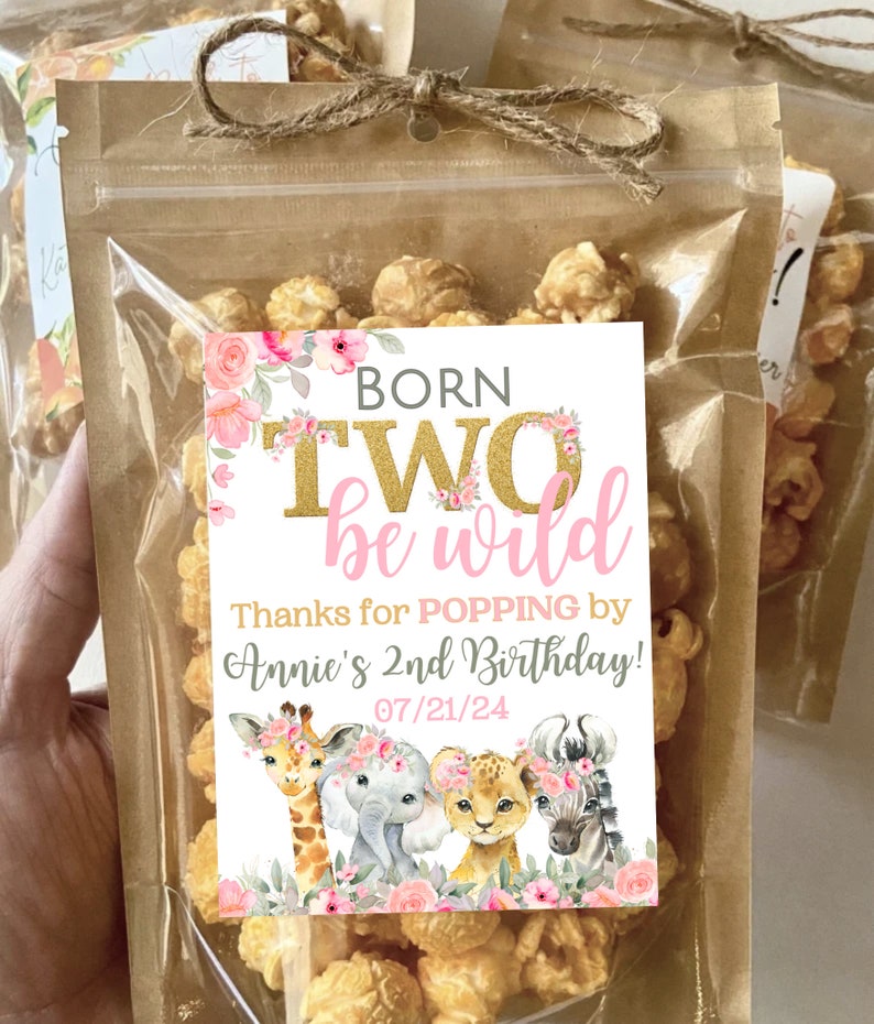 May include: A small clear bag filled with popcorn and tied with twine. A white tag with pink and gold lettering reads "Born Two be wild" and "Thanks for POPPING by Annie's 2nd Birthday! 07/21/24". The tag features a cartoon giraffe, elephant, lion, and zebra with floral accents.