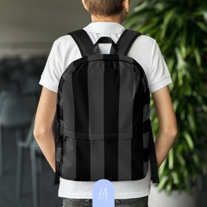 May include: A black and gray striped backpack with adjustable straps. The backpack has a zippered front pocket and a large main compartment.