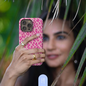 May include: A pink and beige leopard print phone case for an iPhone.