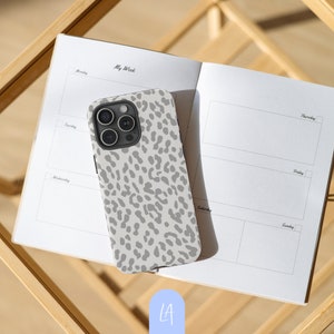 Könnte beinhalten: Eine weiße iPhone-Hülle mit einem grauen Leopardenmuster. Die Hülle hat einen Ausschnitt für das Kameraobjektiv und einen schwarzen Rand.