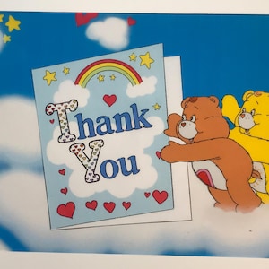 May include: A greeting card with the words "Thank You" in a whimsical font, decorated with hearts and a rainbow. Two cartoon bears are embracing the card against a blue sky background with clouds and stars.